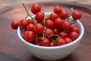 Some tiny cherry tomatoes and green peppers in white plates on wooden concept.