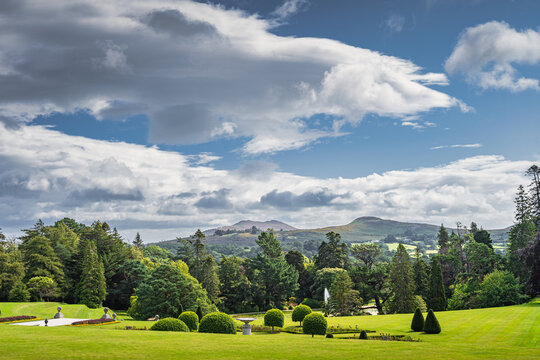 Beautiful garden with flower pots, green lawn and ornate bushes in Powerscourt gardens, forest and Sugerloaf mountain in background, Wicklow, Ireland