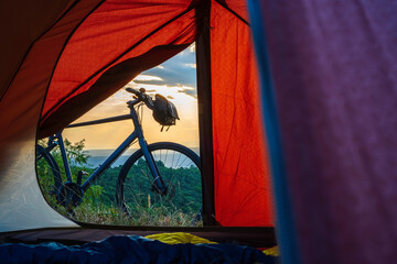 Touring bike seen from inside a tent at sunset by a traveler eager for wilderness adventures. Cycle...