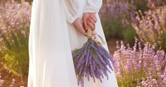 a gentle girl in a white light dress holds a bouquet of lavender flowers