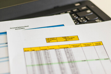 Close up shot of a print outs of excel table of a bank loan amortization table, personal balance sheet and laptop. Banking