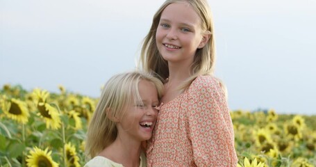 Beautiful little girls enjoying nature . Happy smiling female kids stand in sunflowers field