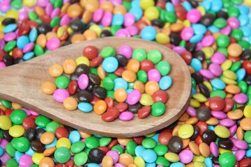 Chocolate candies covered in colored sugar in a wooden spoon, colored background, selective focus, top view.