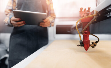 Closeup laser CNC cutting background industry worker using tablet computer for tune and control...