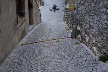 Mountain farmer with spike roller mower at the end of a village alley