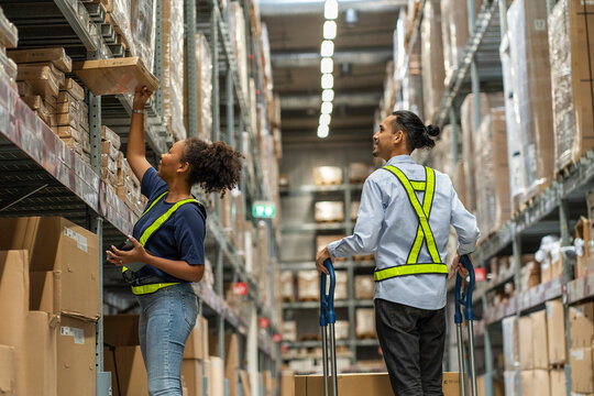  female African American worker picks up a box, checks the price of an item, and an Asian man pushes a logistics truck to a customer.