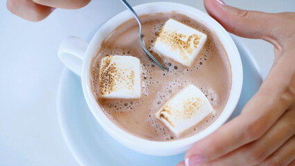 close-up, top view, white cup with cappuccino, with thick creamy foam and marshmallows. a woman's...