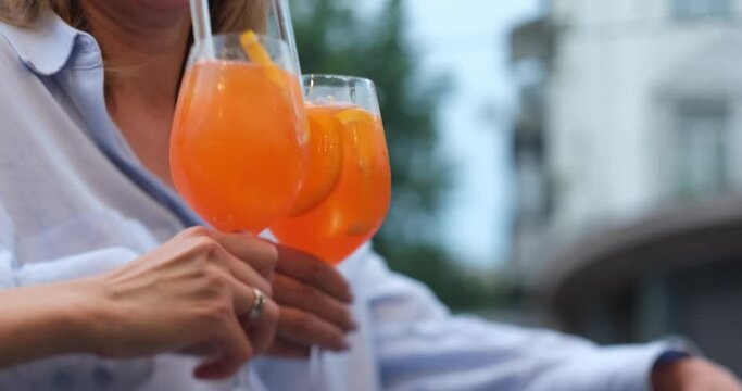 Friends hanging out in a bar clinking with glasses of Spritz cocktail. Aperol spritz cocktail, close up shot. Refreshing alcoholic drink in the hands. No faces. High quality 4k footage