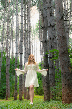 Wide Angle Portrait Of A Pretty Girl In Forest Wearing A White Dress And Looking Upward. 