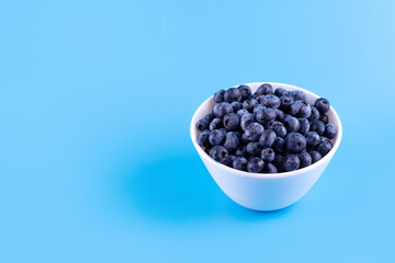 Fototapeta na wymiar Fresh blueberries in white plate on blue background. Vegan and vegetarian concept. Summer healthy food. Flatlay.