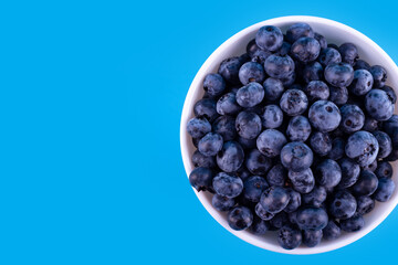 Fresh blueberries in white plate on blue background. Vegan and vegetarian concept. Summer healthy food. Flatlay.