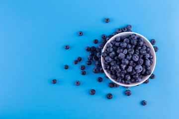 Fresh blueberries in white bowl on blue background. Flat lay, top view..Vegan and vegetarian concept. Summer healthy food.