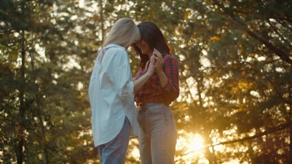 Two young women lesbian couple hugging and holding hands at sunset. Tender relationship of a loving homosexual couple - Powered by Adobe