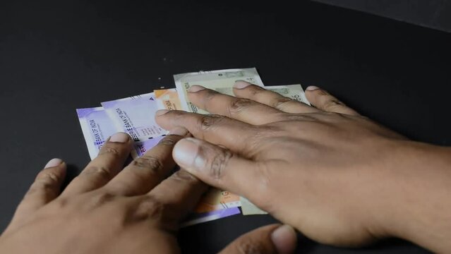 A close up video of a man grabbing Indian currency Notes against a black Background