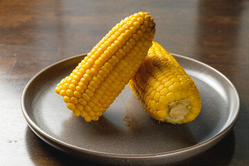 Close view on Homemade sweet corn cobs with salt in bowl on  wooden table