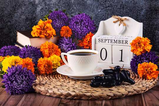The first of September, the beginning of autumn, a day in the calendar. Autumn composition with asters, marigolds, books, grapes and a cup of coffee on the table. Hello autumn. Side view.