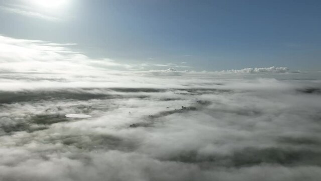 Flying above clouds over hills. above fog on a farm landscape below. mist covering the mountains in the country 