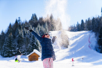 Happy child throwing snow on sunny winter day outdoor. Kid having fun at snowy ski resort, enjoying...