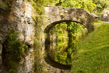 Old bridge over a canal with reflections of the bridge and trees on the still water