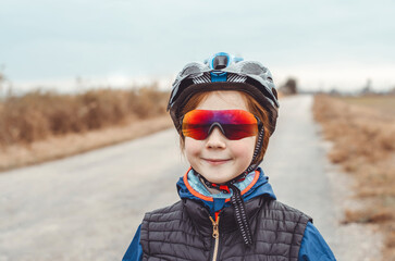 Portrait of an 11-year-old girl cyclist, traveler. Girl in a protective sports helmet and sports goggles on a country road