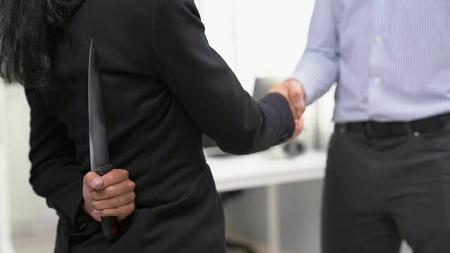 Back view of businesswoman shaking hands with another businessman while holding a knife behind his back. Concept of back backstabbing in business, backstabbing between colleagues.