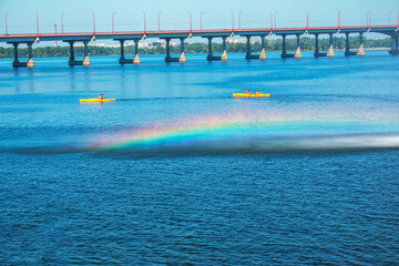Athletes in kayaks in training near the river fountain in a rainbow of splashes.
