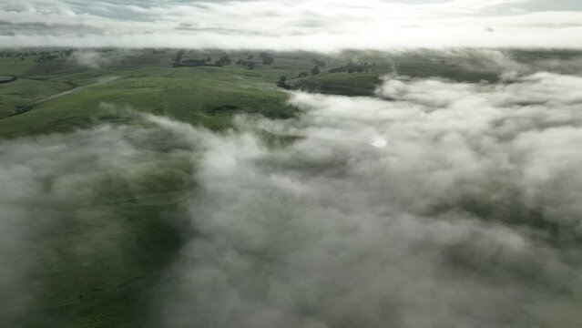 Flying above clouds over hills. above fog on a farm landscape below. mist covering the mountains in the country 