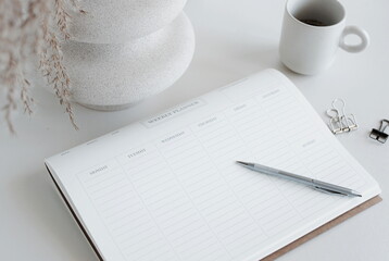 weekly planner mockup with copy space on home desk workspace with modern vase, pen, cup coffee top...