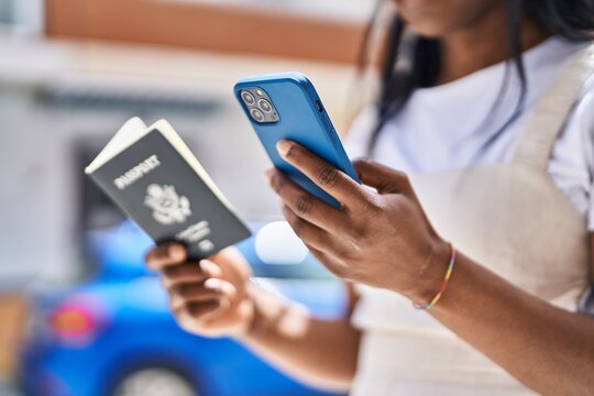 Young african american woman using smartphone holding united states passport at street