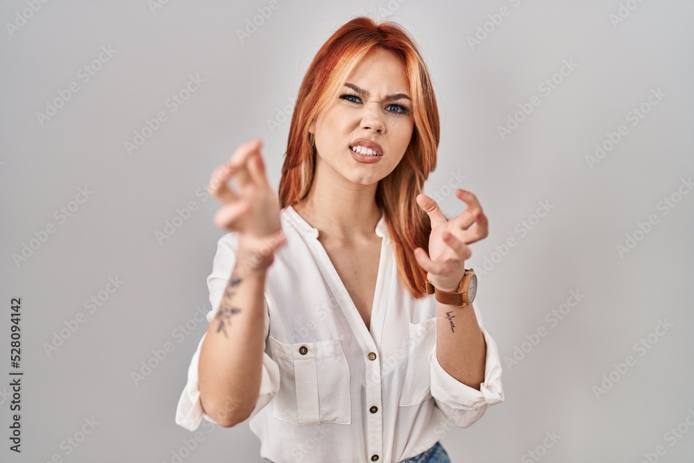 Sticker Young caucasian woman standing over isolated background shouting frustrated with rage, hands trying to strangle, yelling mad