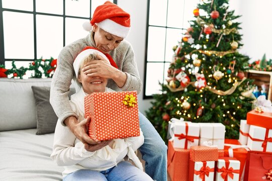 Senior man suprising his wife with christmas gift at home.