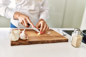Obraz na płótnie Canvas Young blonde woman cutting garlic at kitchen