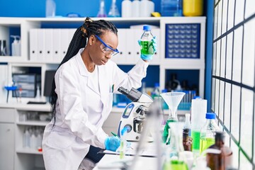 African american woman scientist holding bottle write on document at laboratory
