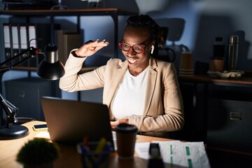 Beautiful black woman working at the office at night gesturing with hands showing big and large size sign, measure symbol. smiling looking at the camera. measuring concept.