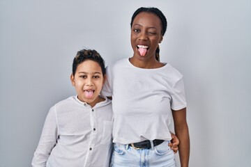 Young mother and son standing together over white background sticking tongue out happy with funny expression. emotion concept.