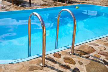 Ladder stainless steel handrails for descent into swimming pool. Clear blue water in the pool....