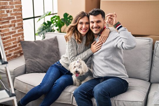 Man and woman holding key sitting on sofa with dog at new home
