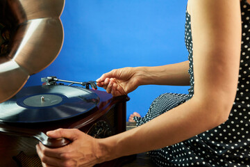 A young beautiful woman in black cocktail dress in polka dots puts a pin on the vinyl. Close up...