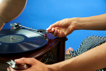 A young beautiful woman in black cocktail dress in polka dots puts a pin on the vinyl. Close up view of the hand and vinyl player. The record is playing in the player. Old style concept