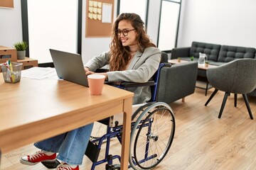 Young beautiful hispanic woman business worker using laptop sitting on wheelchair at office