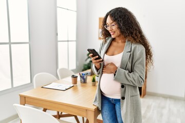 Young latin woman pregnant smiling confident using smartphone working at office