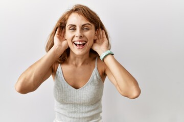 Beautiful caucasian woman standing over isolated background trying to hear both hands on ear gesture, curious for gossip. hearing problem, deaf