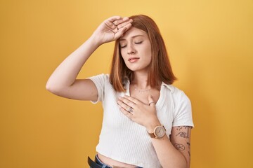 Young redhead woman standing over yellow background touching forehead for illness and fever, flu and cold, virus sick