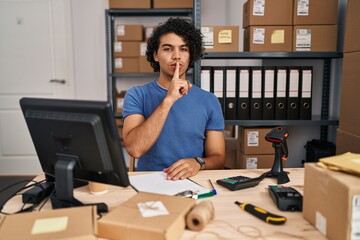 Hispanic man with curly hair working at small business ecommerce asking to be quiet with finger on...