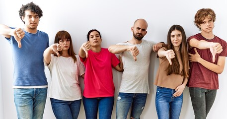 Group of young friends standing together over isolated background looking unhappy and angry showing rejection and negative with thumbs down gesture. bad expression.