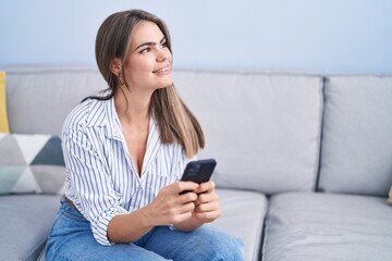 Young woman using smartphone sitting on sofa at home