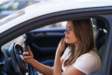 Fototapeta na wymiar Young woman talking on the smartphone sitting on car at street