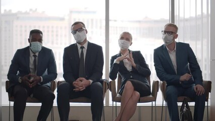 Multiethnic people in safety face mask sit in business center waiting room. Realtime