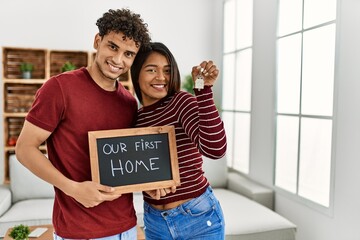 Young latin couple smiling happy holding our first home blackboard and key at house.