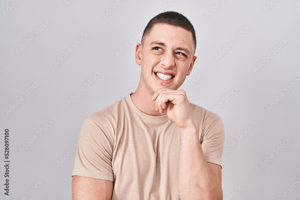 Sticker Young man standing over isolated background thinking worried about a question, concerned and nervous with hand on chin